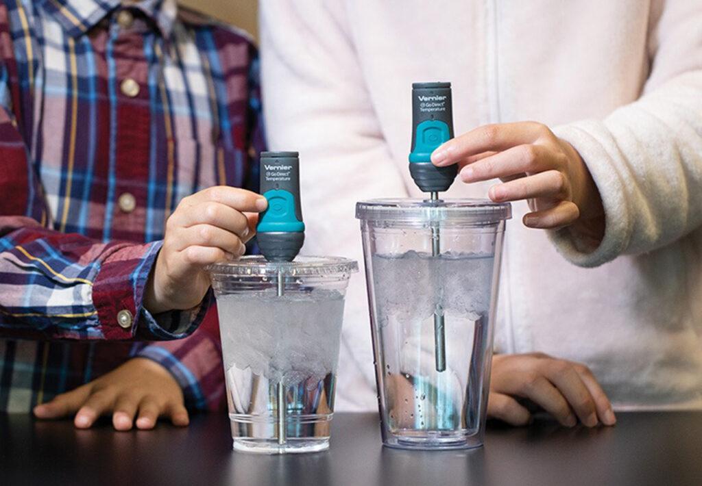 Two students each hold a Go Direct Temperature Probe over a glass of ice water, the tip of each probe is submerged